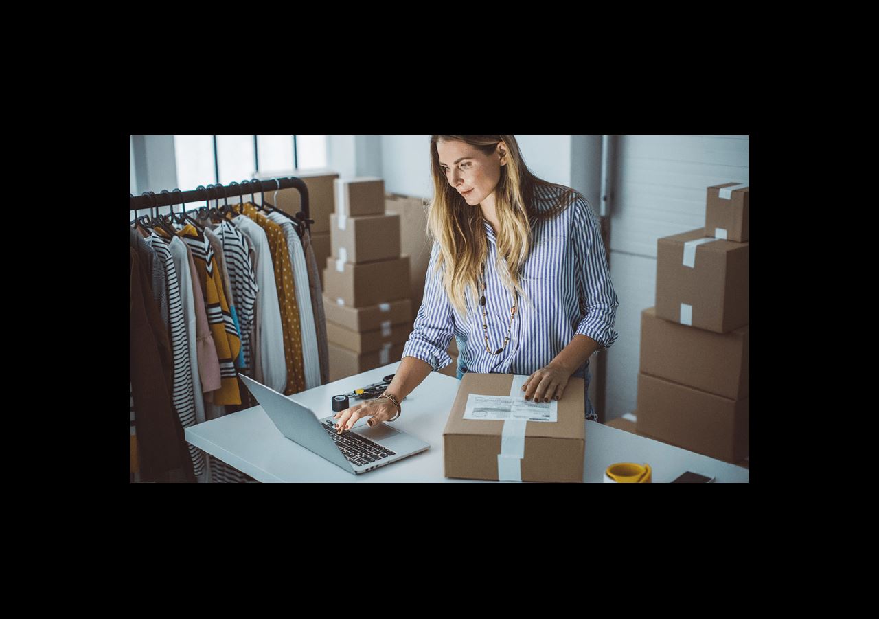 Woman looking at her laptop and preparing a box to ship.