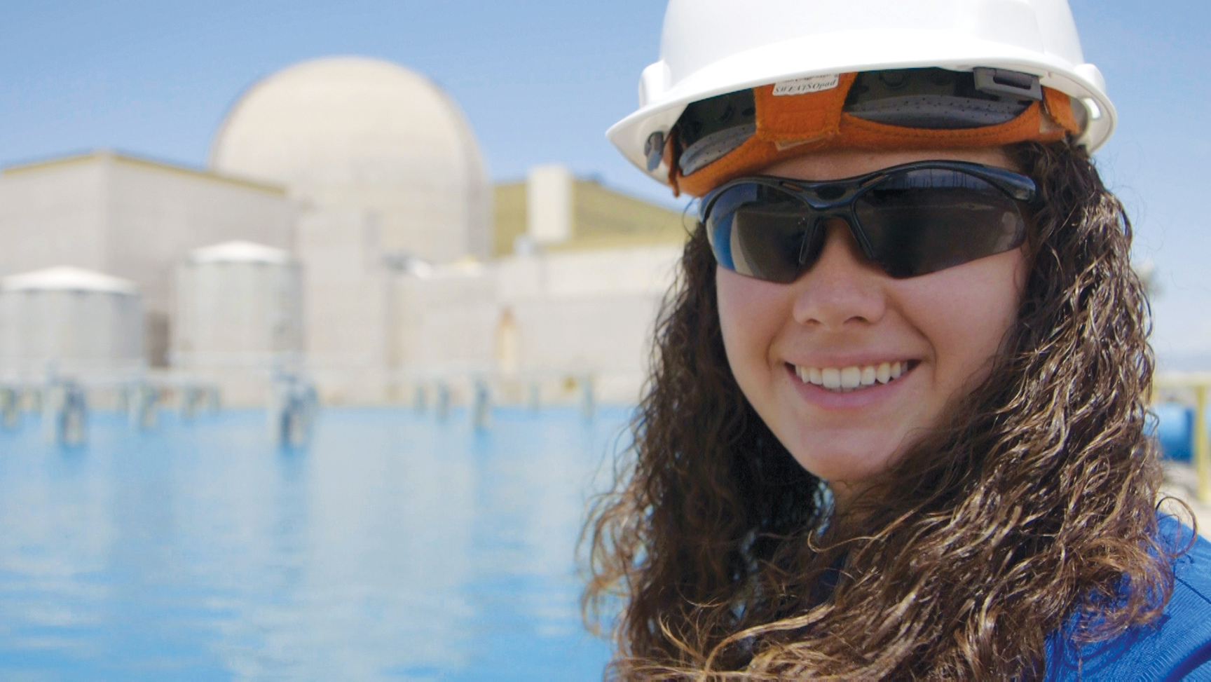 APS employee in protective glasses and a hard hat smiling in front of Palo Verde.