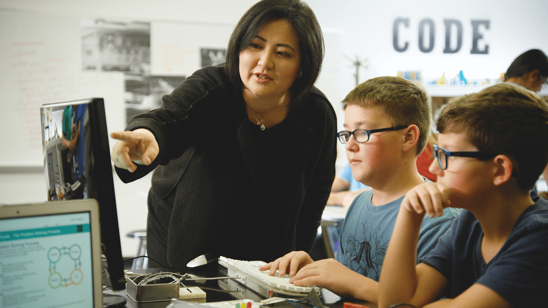 Teacher helping two young students as they work on the computer.