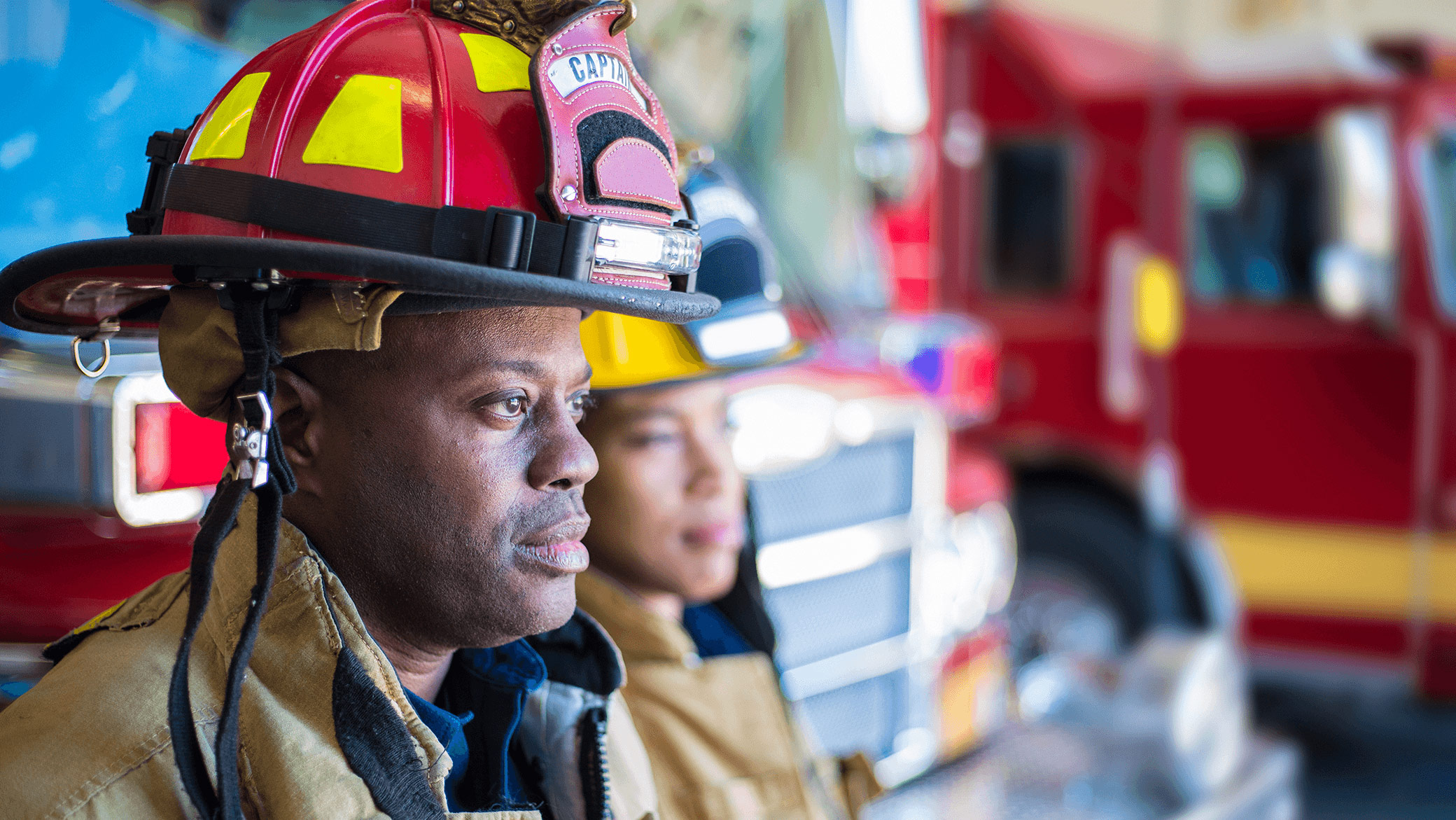 Two fire fighters sitting near their truck, looking outside.