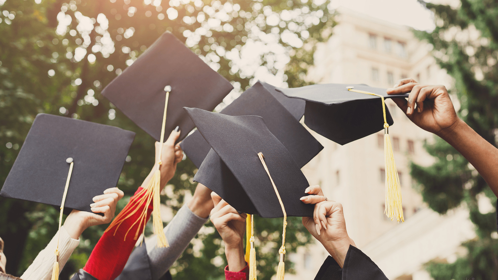 Recent graduates holding their caps together.