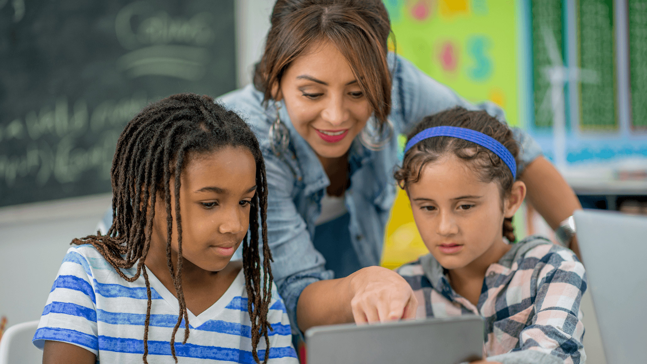 Teacher showing two young students something on a tablet. 