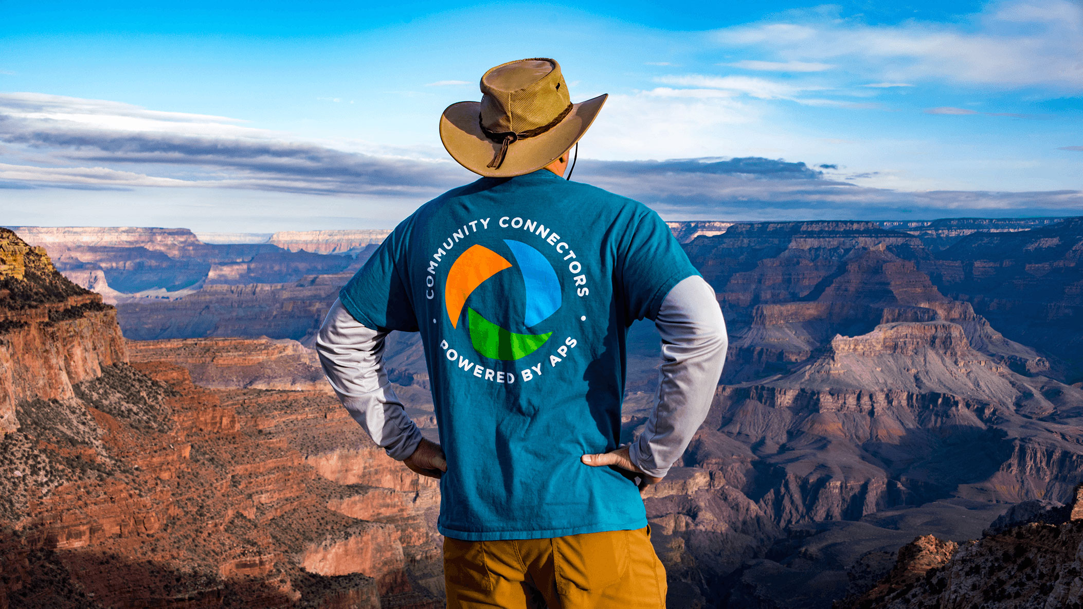 APS employee standing on mountain wearing community connectors branded shirt.