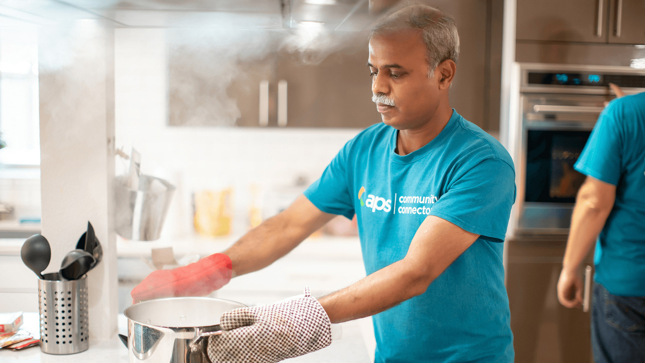 APS employee wearing volunteer shirt cooking in kitchen.