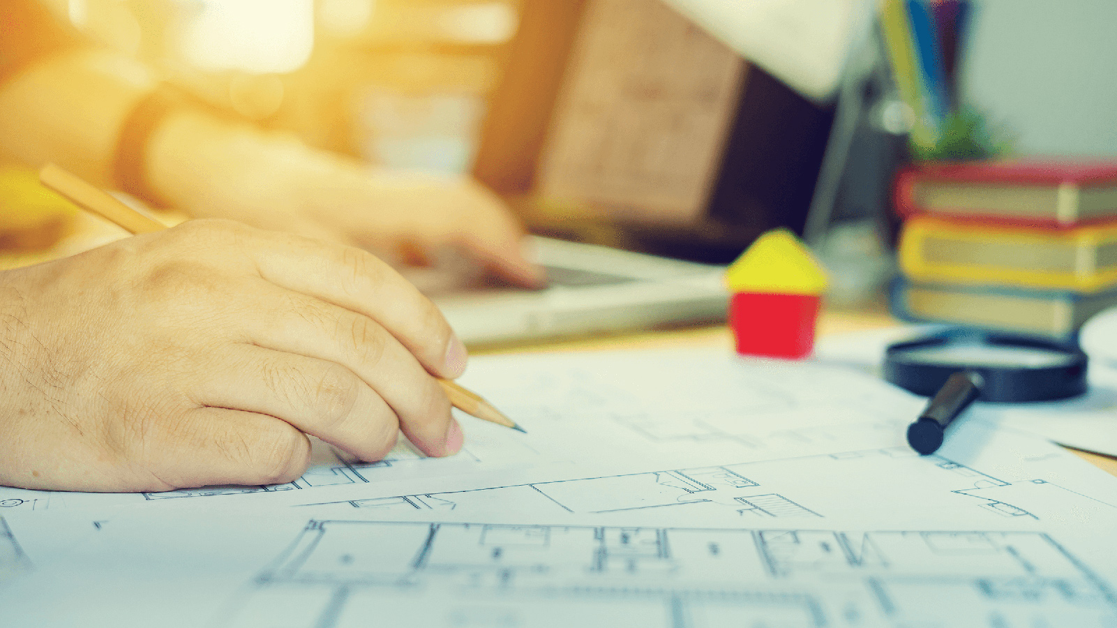 Man drawing a building blueprint and working on his computer.