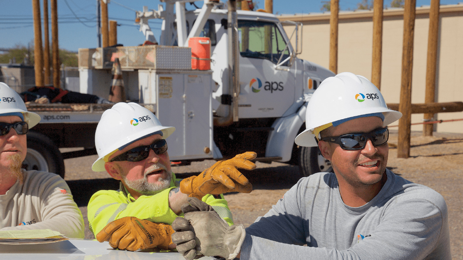 Three APS employees smiling and pointing in front of an APS truck.