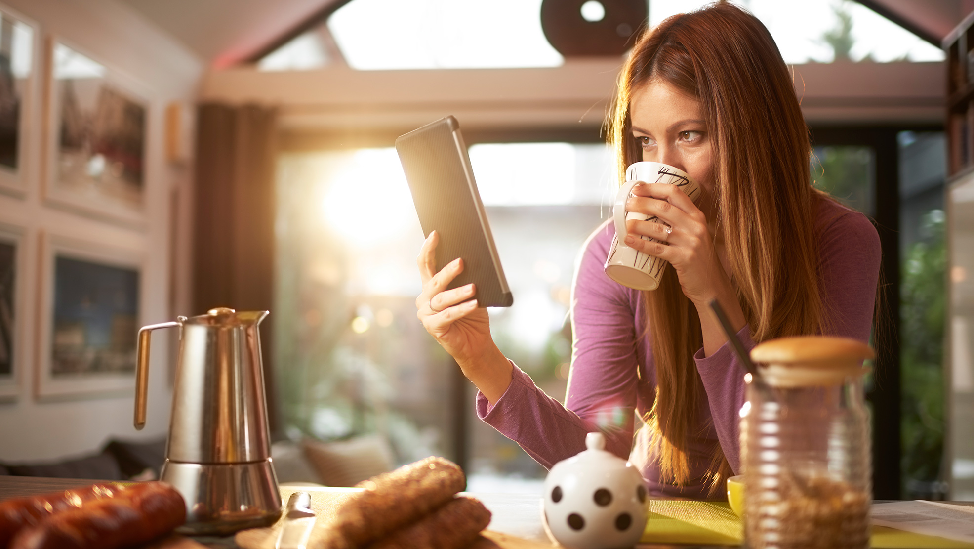 Person drinking morning coffee and looking at tablet.