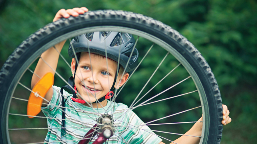young boy wearing a bike helmet holding on to a bicycle wheel