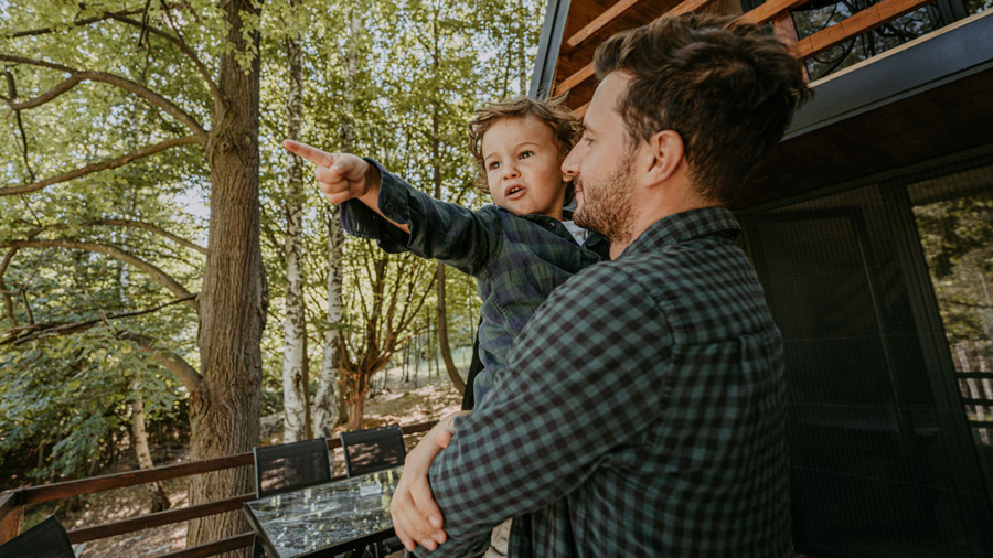 Father holding his child on a patio, looking out into the forest.