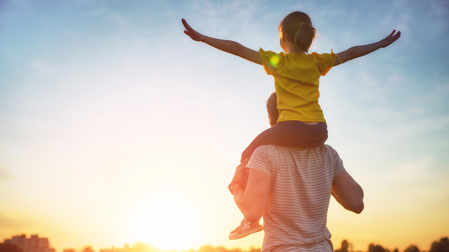 Child sitting on parents shoulders watching the sunset.