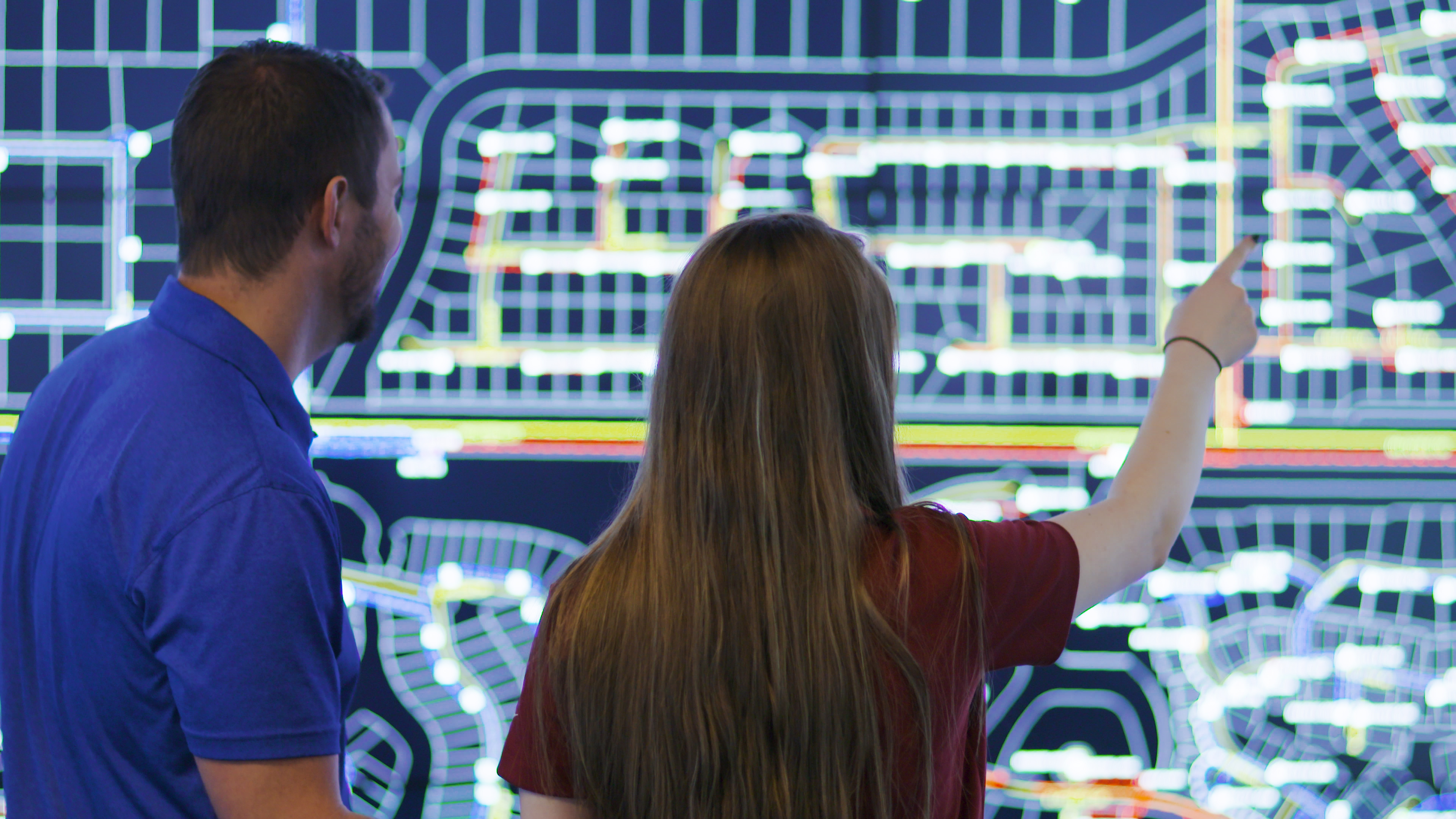 Two employees in front of a digital screen board