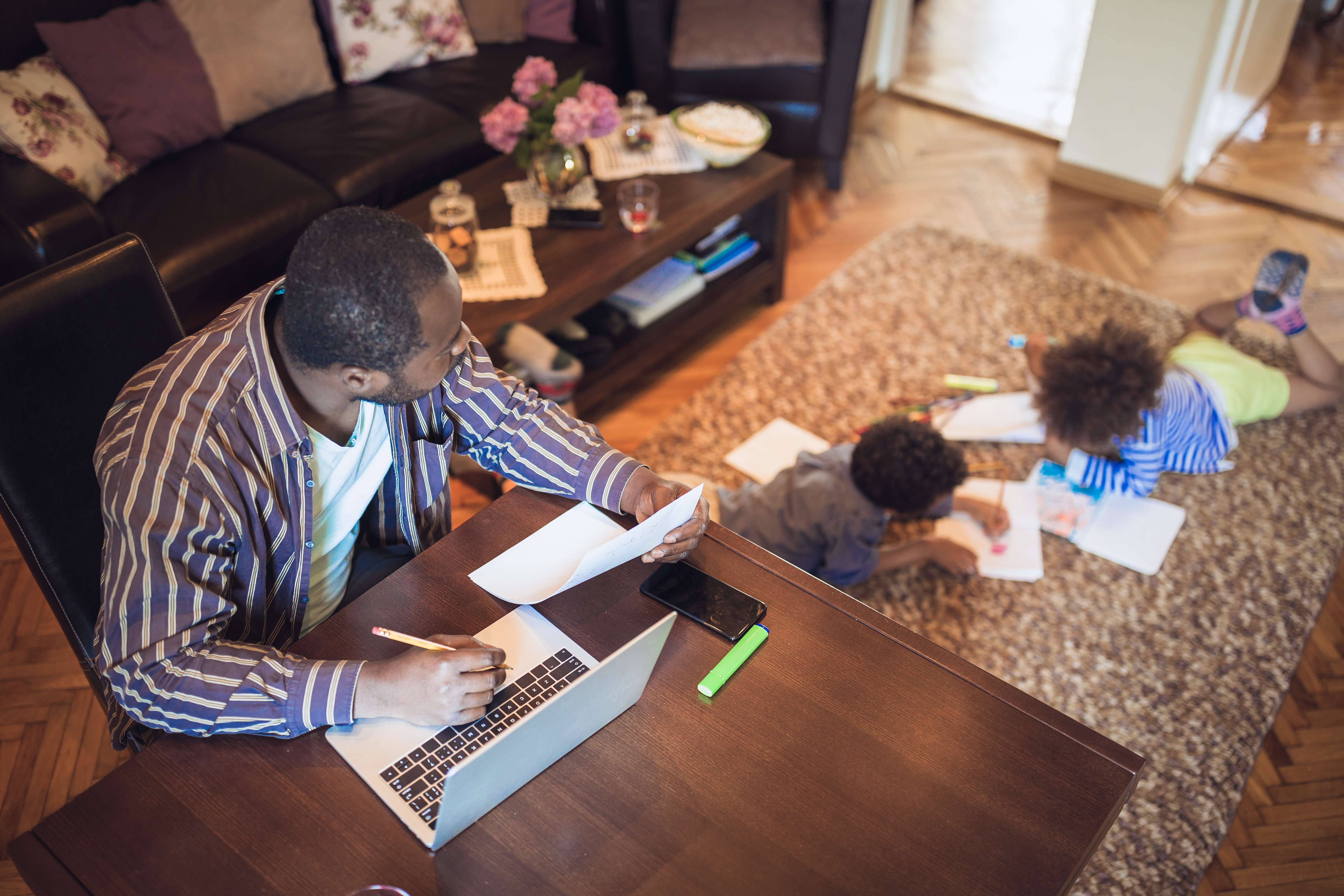 Dad doing bills while his son plays in the room behind him