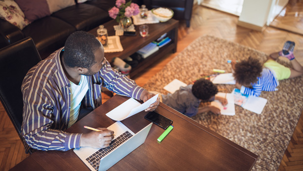 Dad paying bills at a table while his son plays behind him