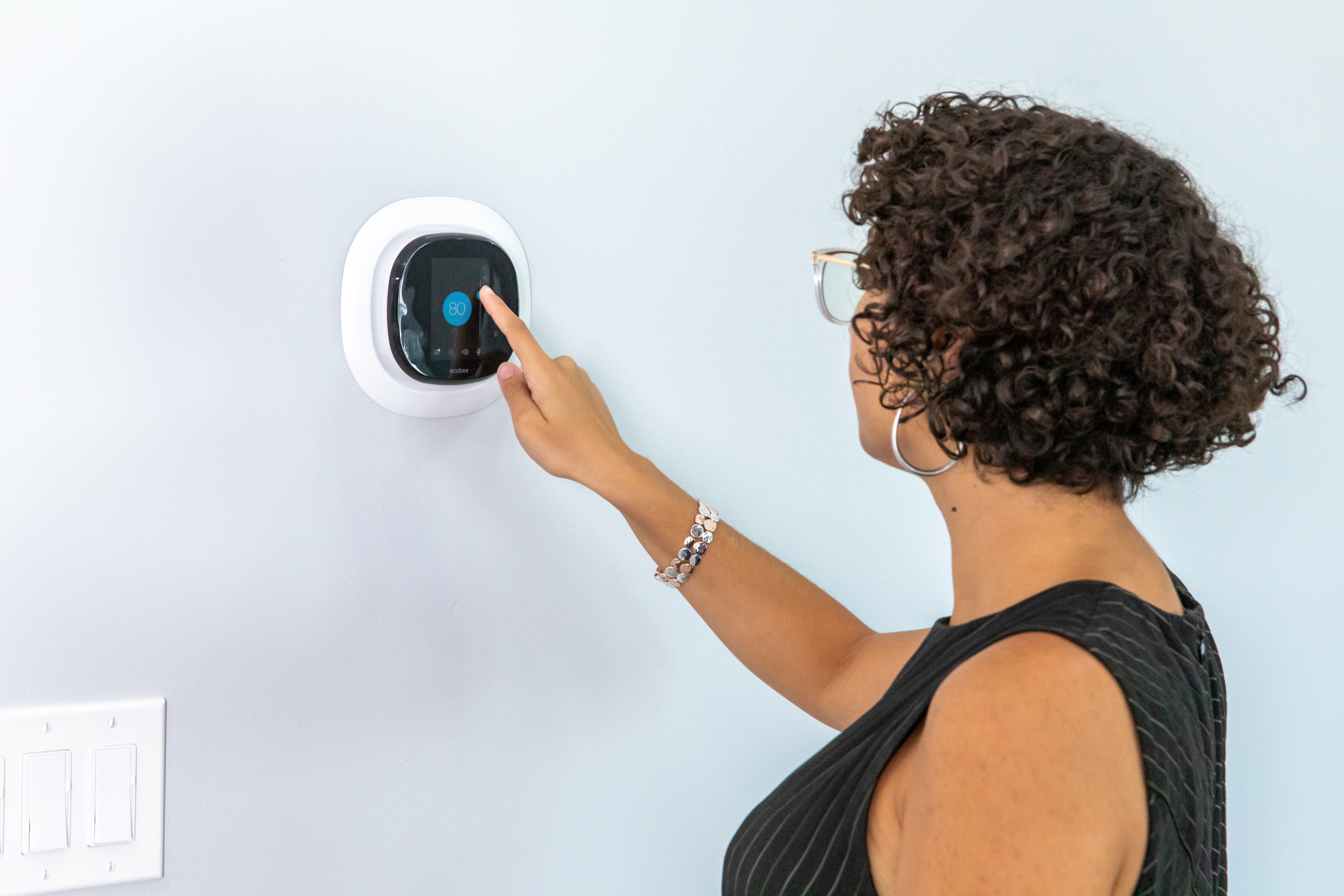 A woman adjusting an Ecobee Smart thermostat