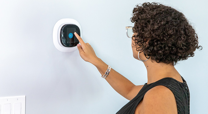 A woman adjusting an Ecobee Smart thermostat