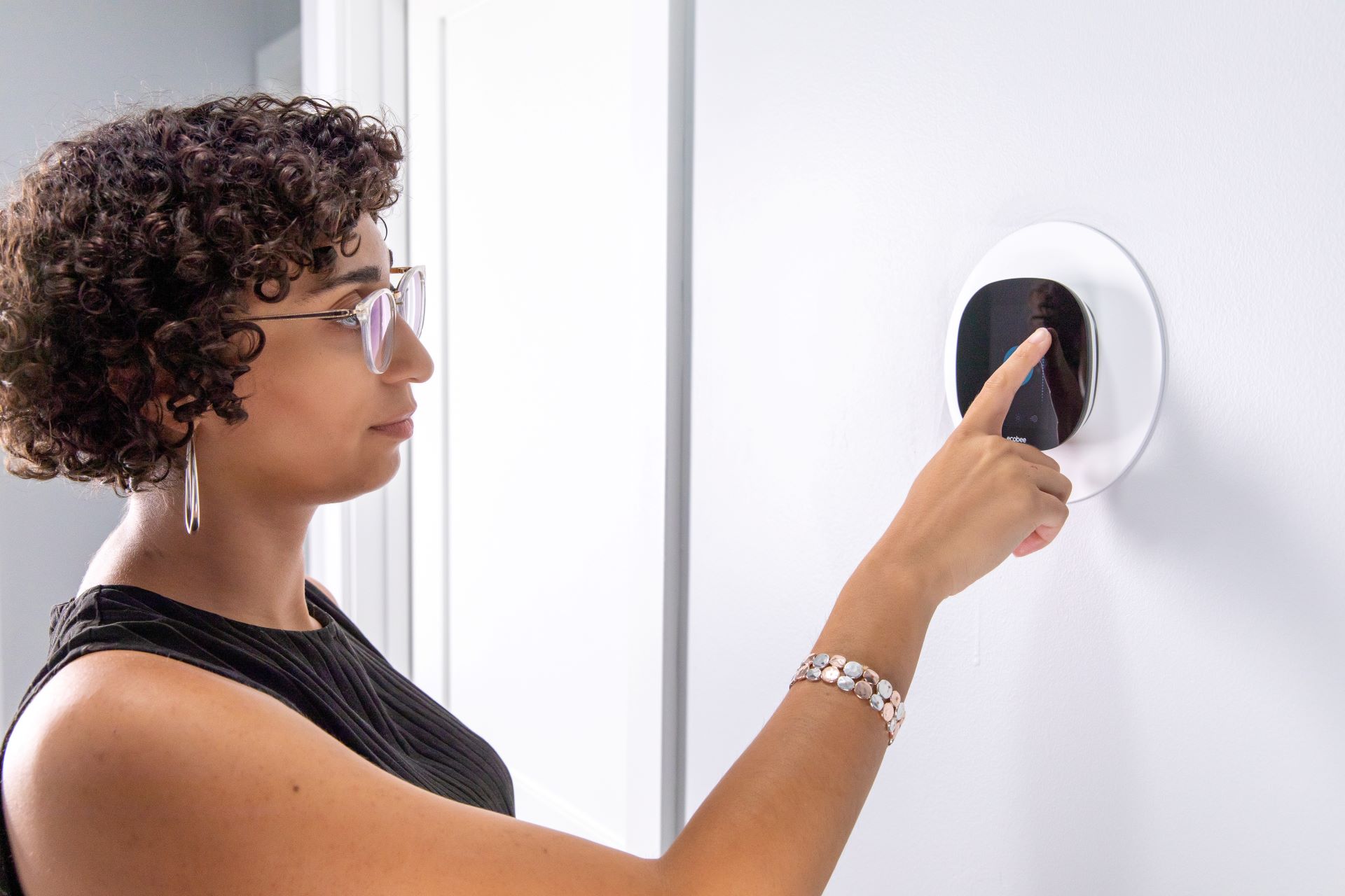A woman adjusting a thermostat in the hallway