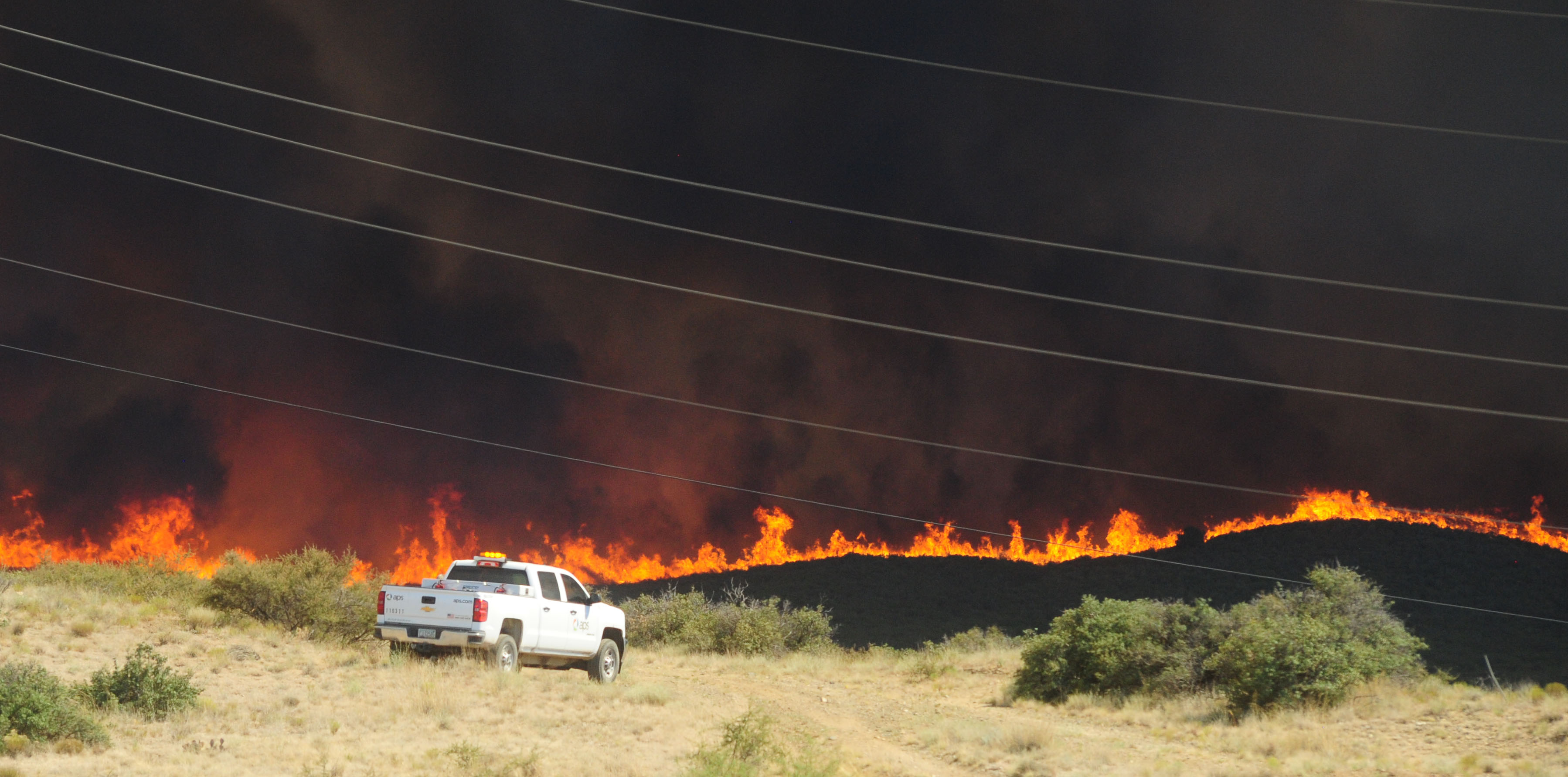 view of a wildfire in the close distance with an APS truck parked on a hill