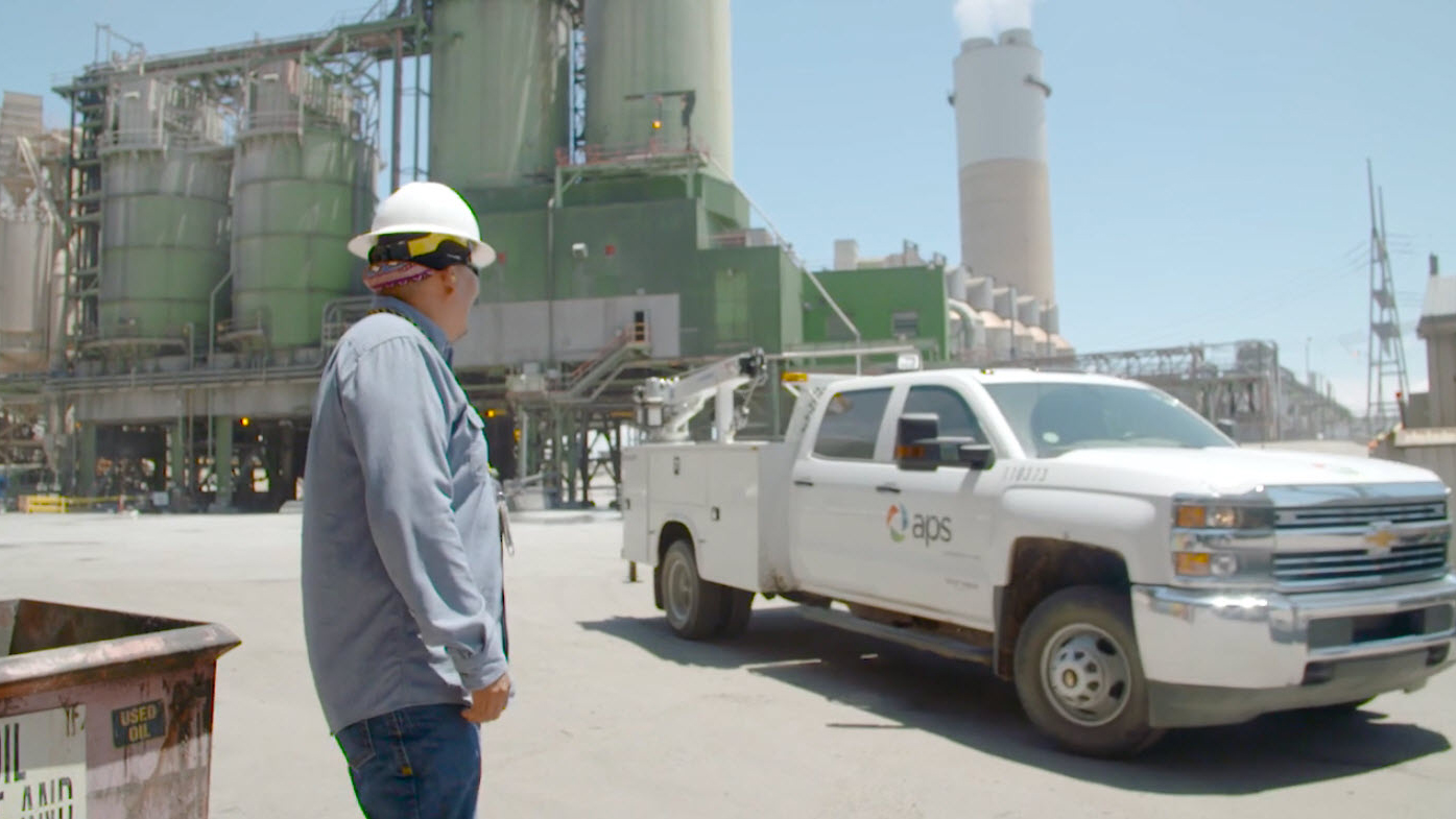 Employee stands outside at the Four Corners Power Plant with APS work truck driving by