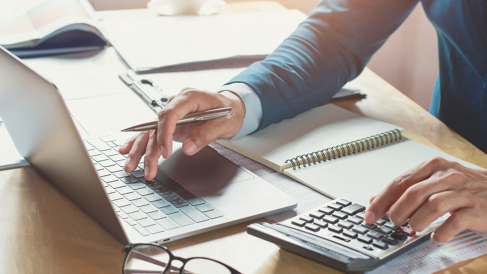 Up close shot of man using a laptop and calculator.