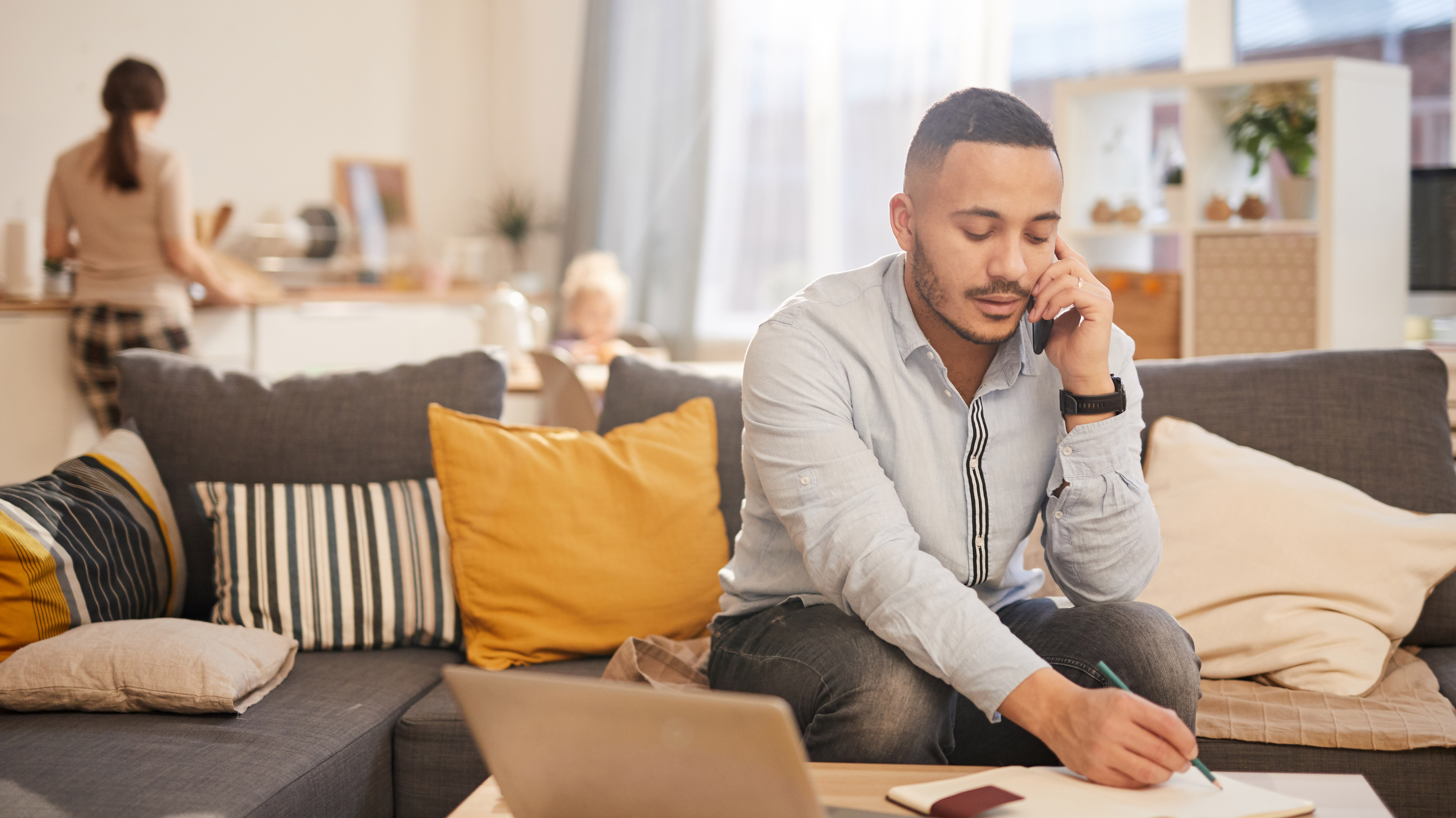 Man sitting on the couch on the phone writing on paper