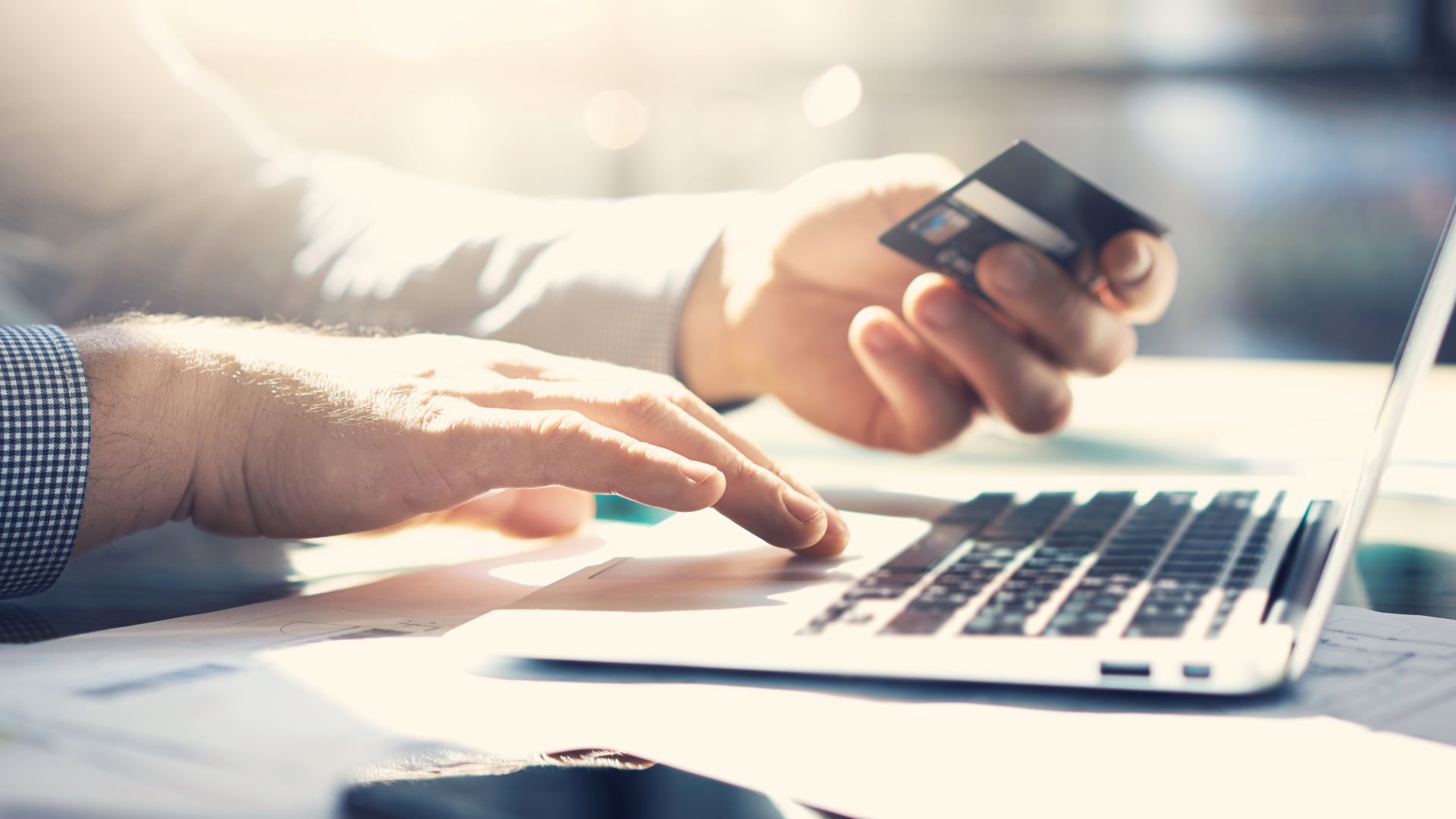 Man holding a credit card while typing on a tabptop