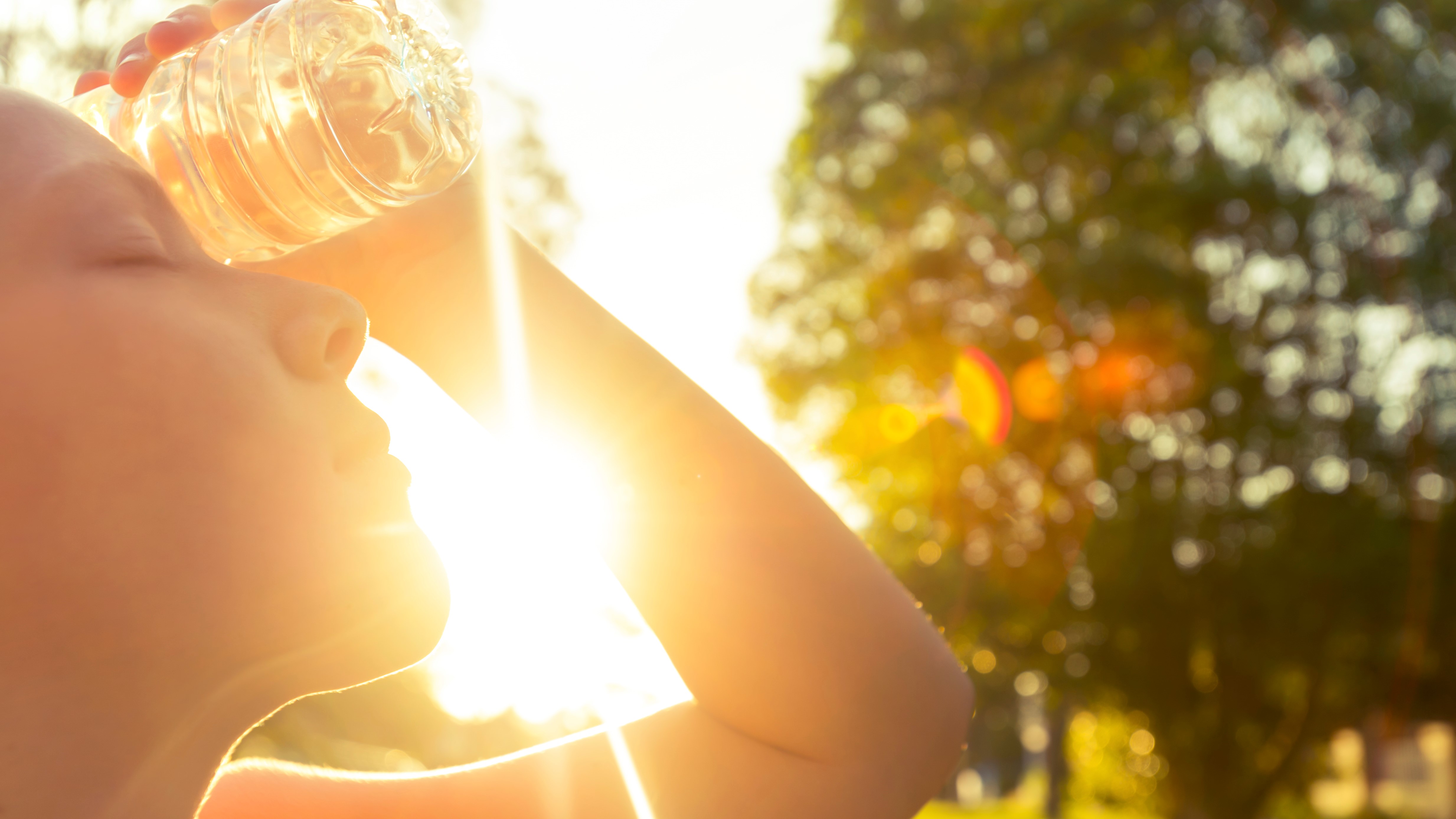 Woman standing outside in the sun holding a water bottle on her forehead to cool down 