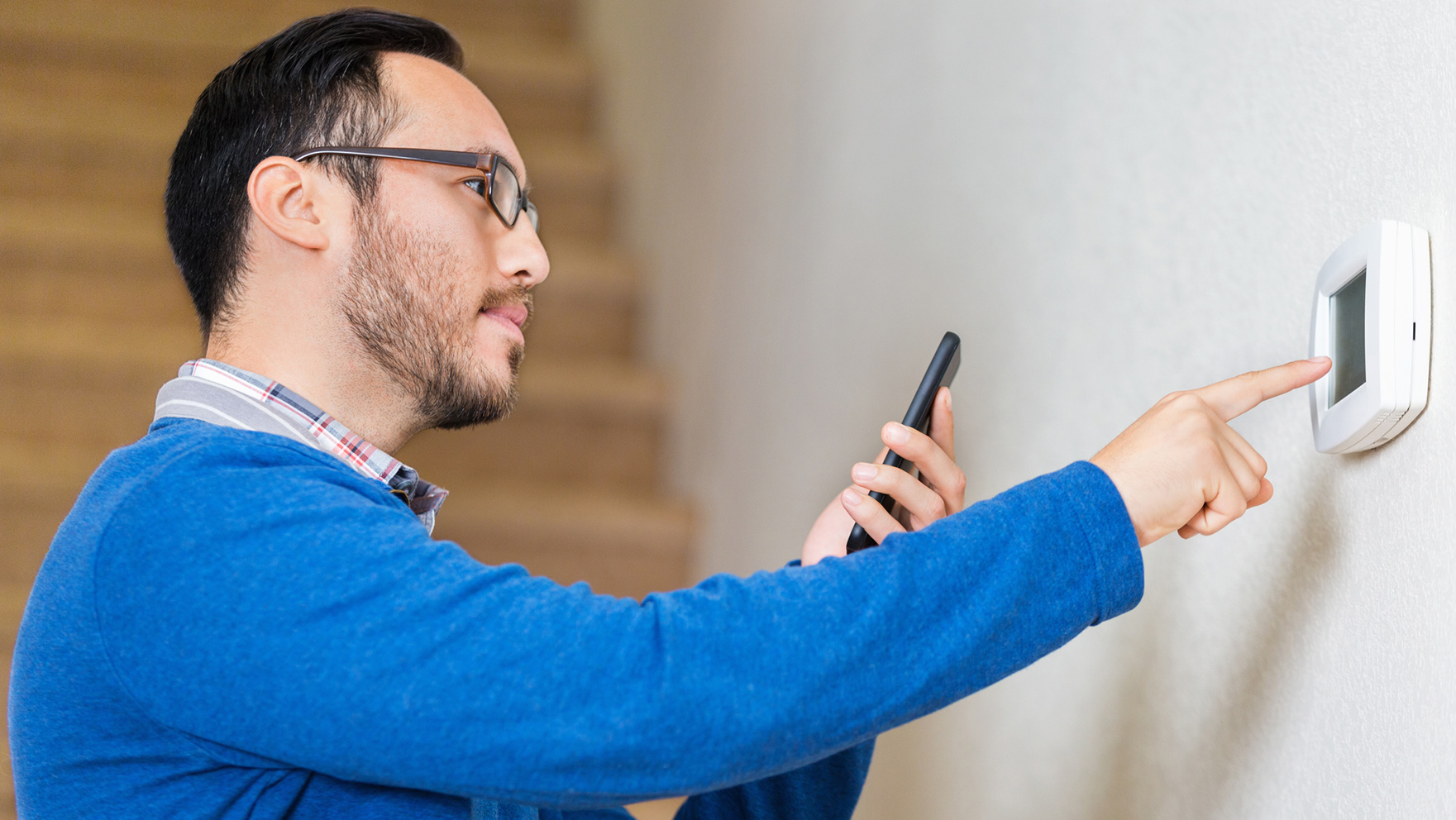Man in blue shirt programming his thermostat.