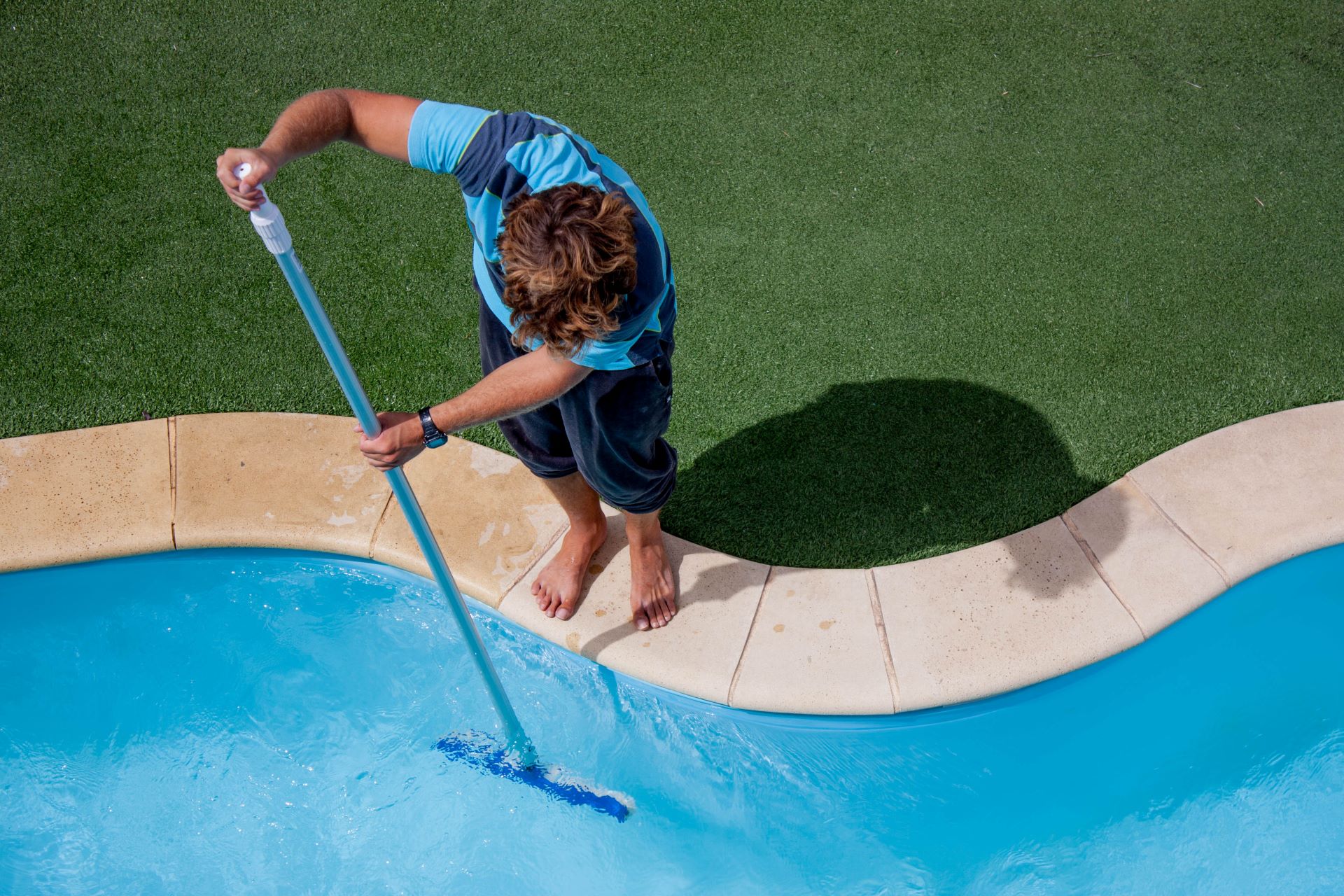 Overhead view of a man brushing the sides of a pool 