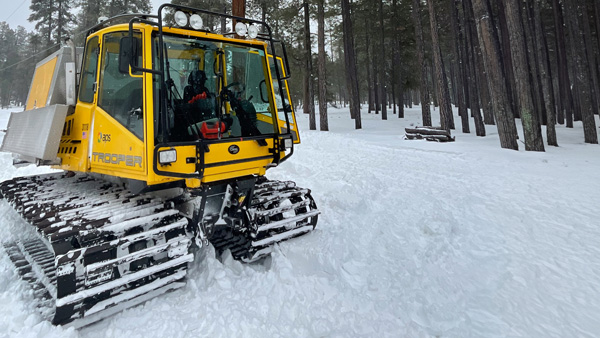 APS Lineman on a pole during a winter storm with a snowcat in the foreground