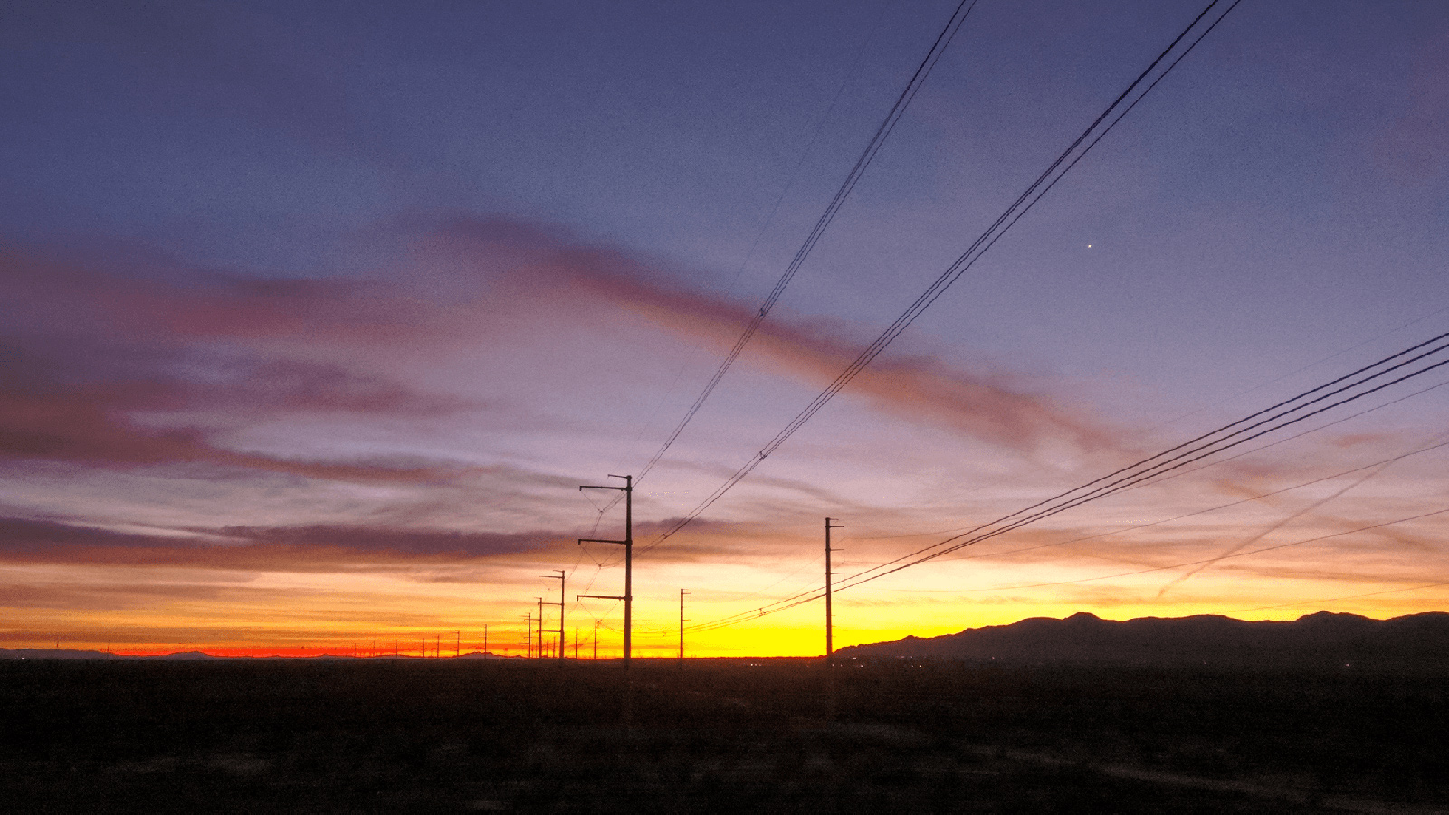 Rural power lines against a purple and yellow sunset.