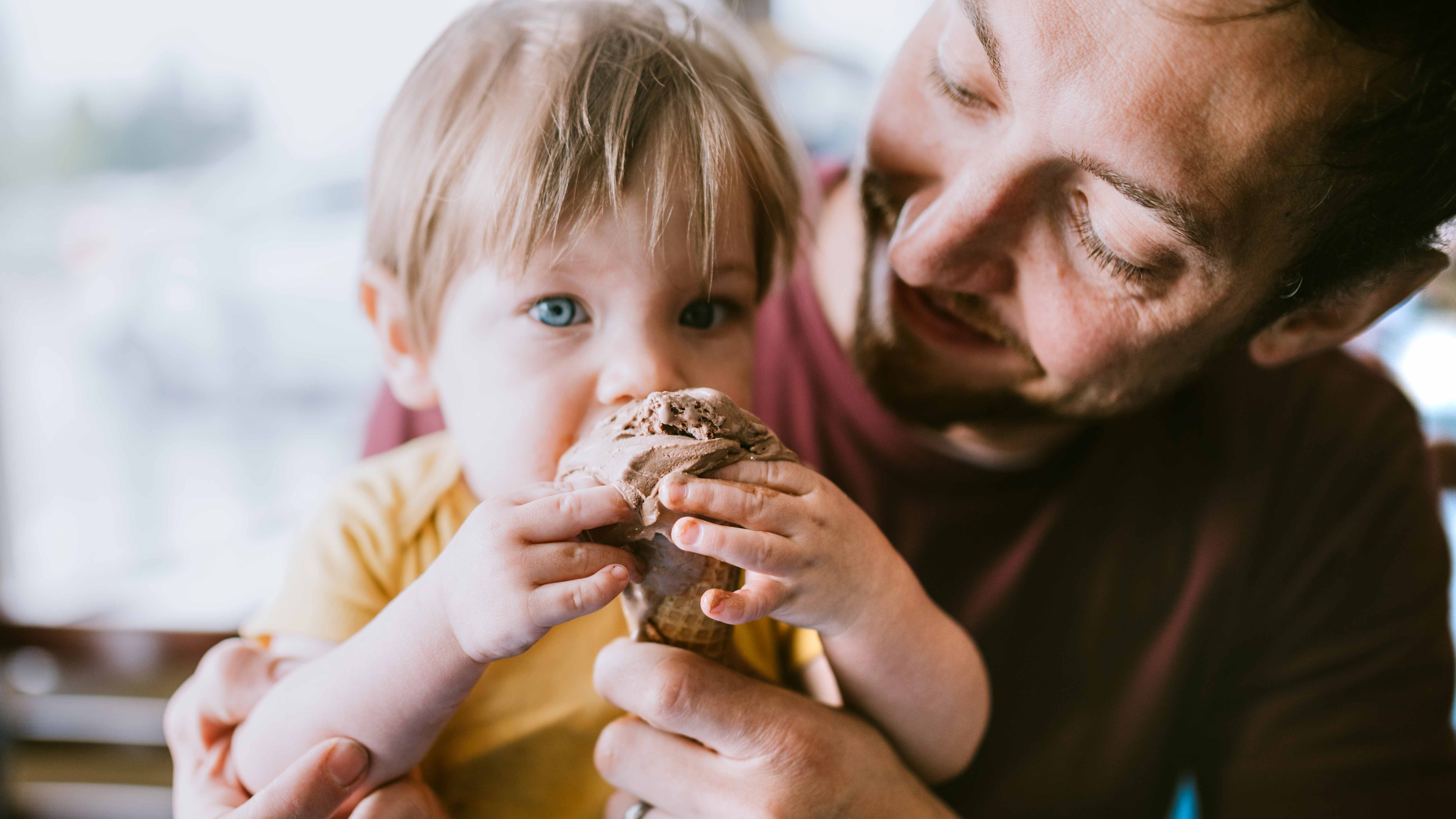 parent holding and helping a young child eat an ice cream cone