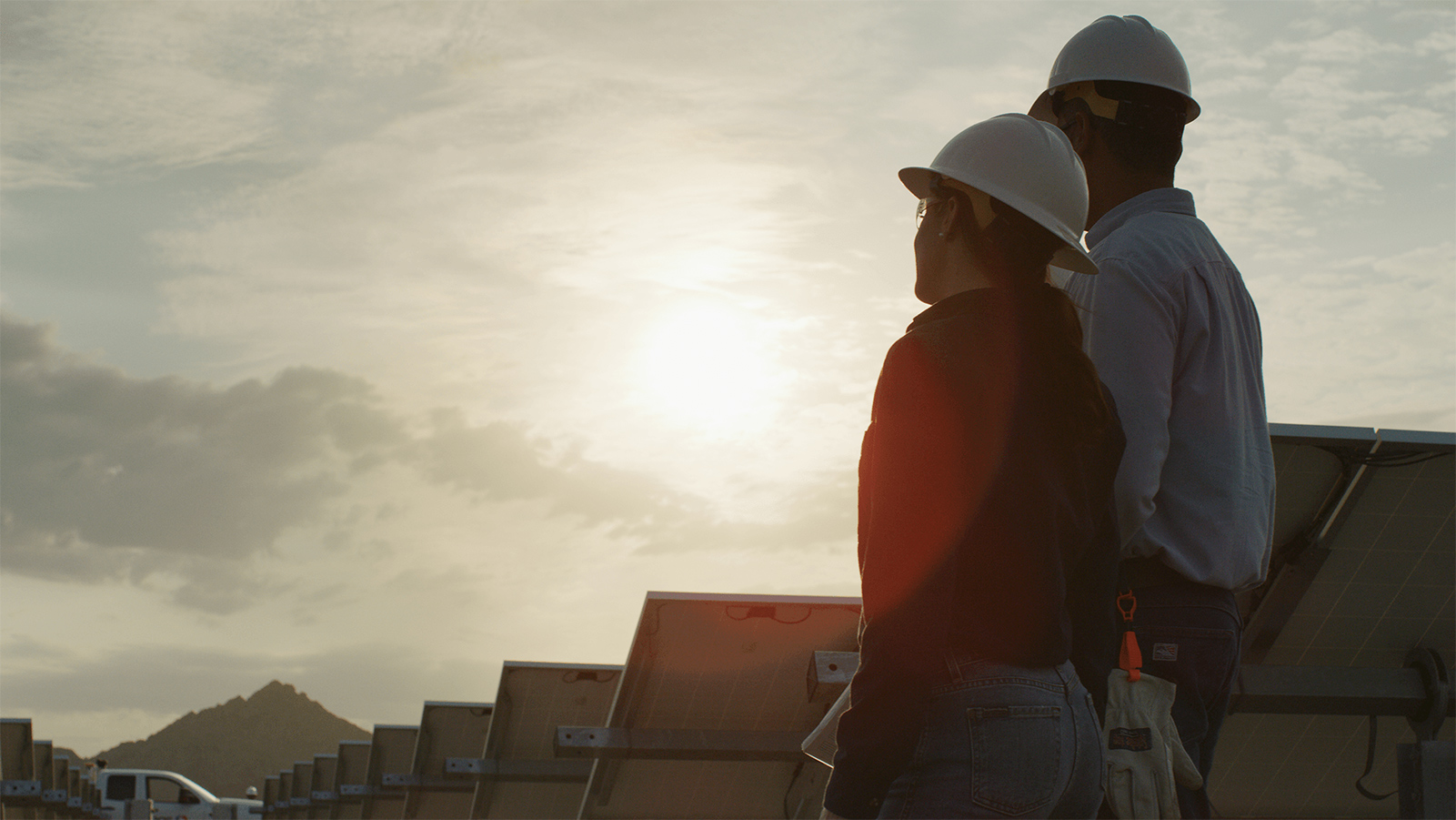 Two APS employees standing behind solar panels.