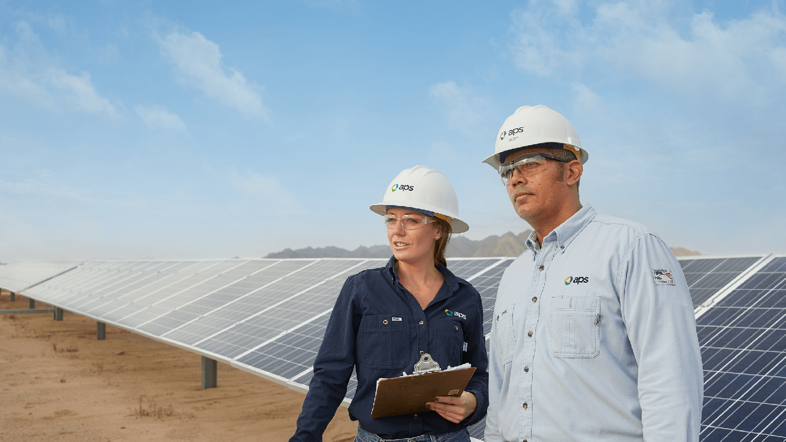 Two APS employees looking into the distance in front of soalr panels.