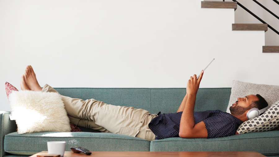 Man lying on couch reading a tablet.