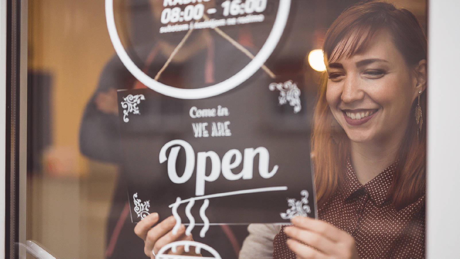 Woman smiling, putting an open sign in a storefront window.
