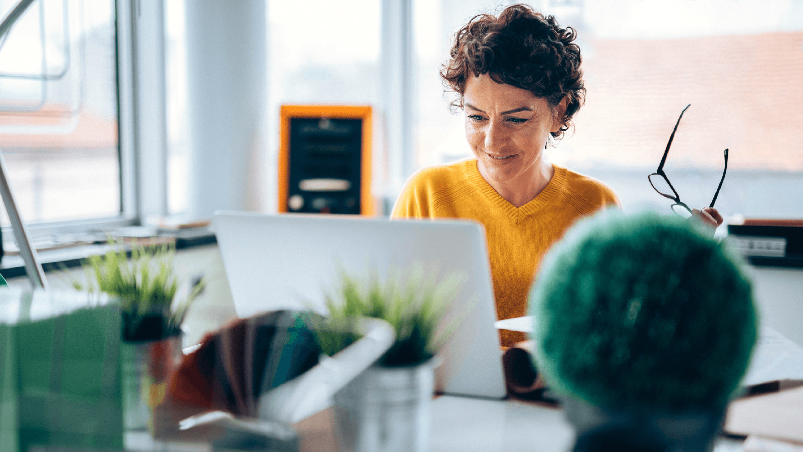 Woman holding her glasses and smiling at her laptop.