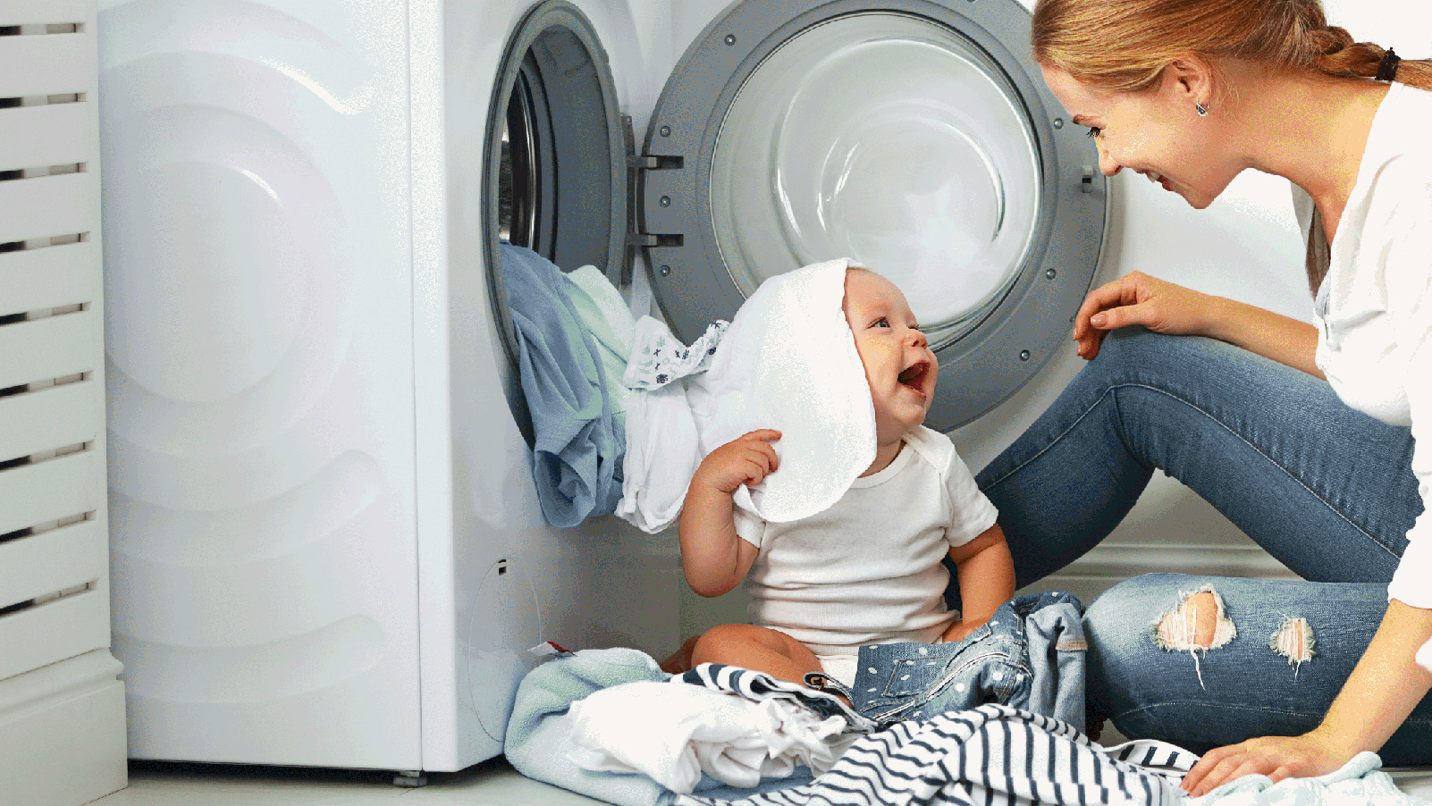 Mother and her baby smiling and playing in the laundry room.