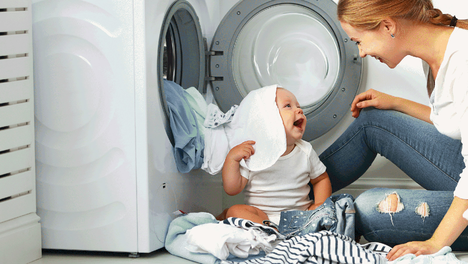 Mother and her baby smiling and playing in the laundry room.