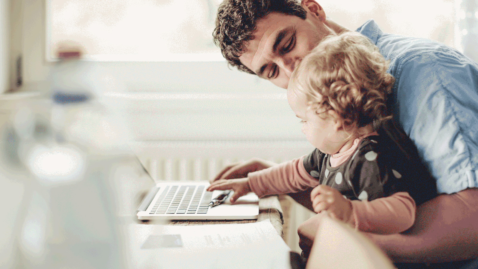Smiling father holding his toddler at a desk with a laptop.