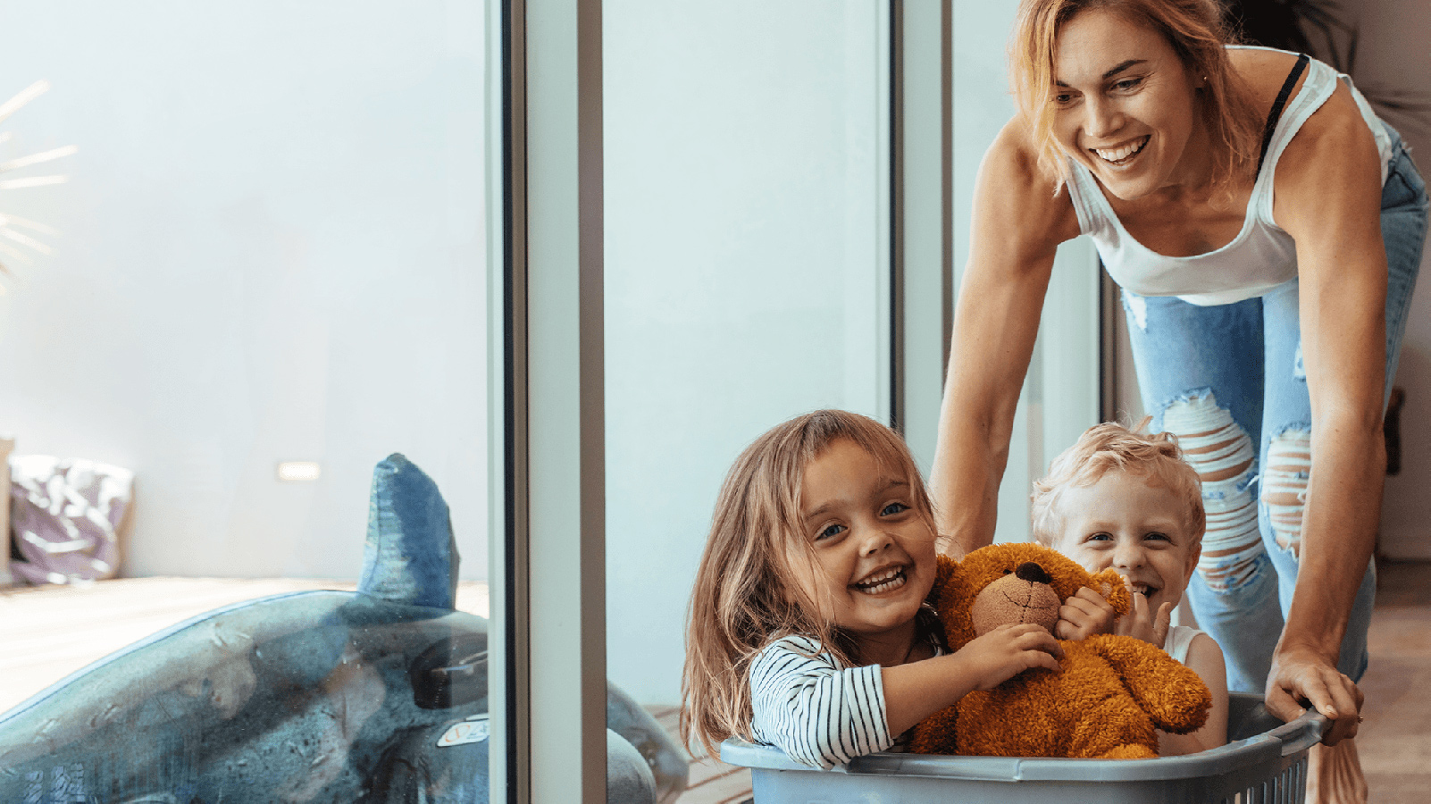 Mother playing with her two kids in a laundry basket.