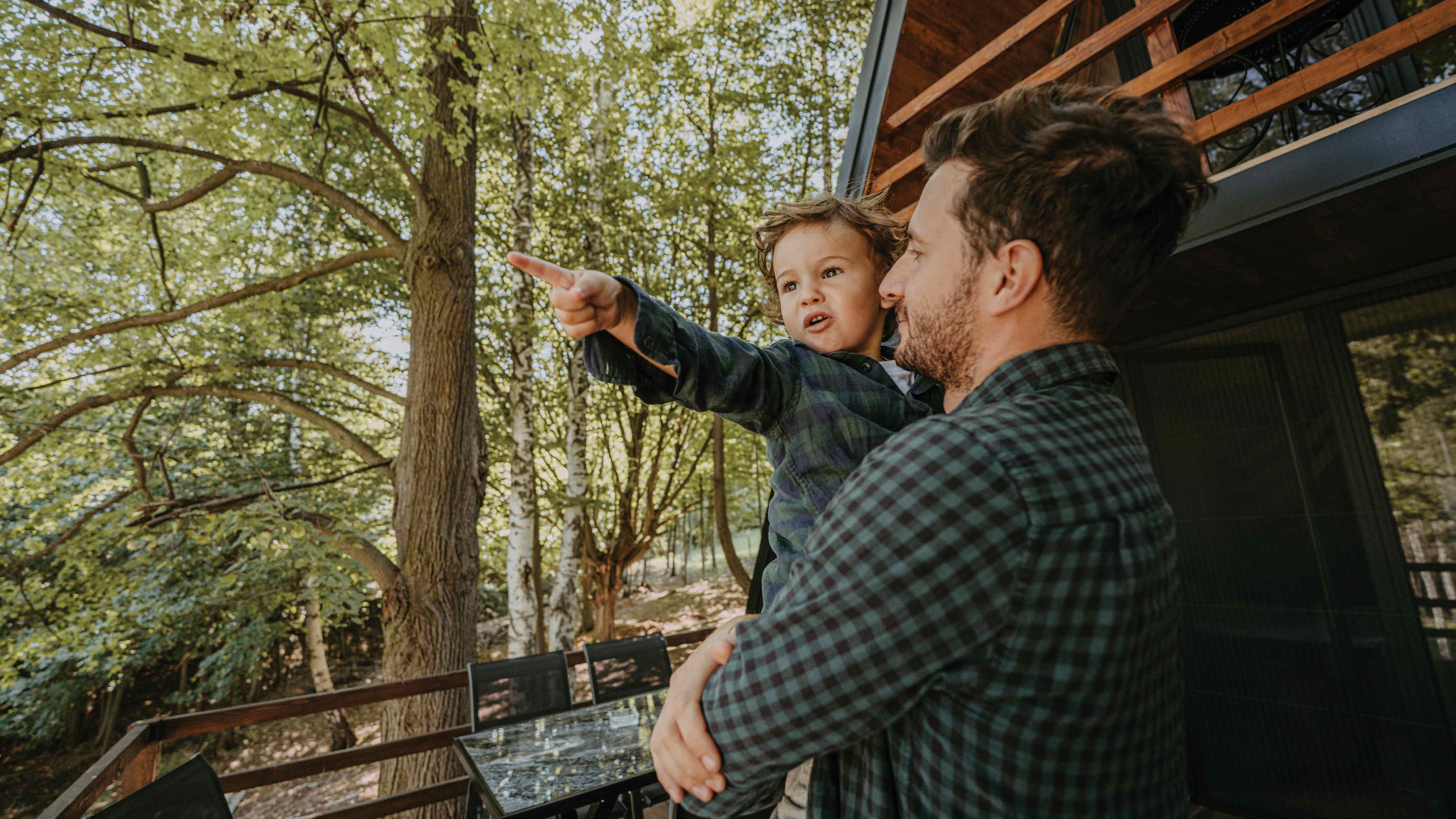 Dad hold a young boy on the porch on of a cabin in the woods