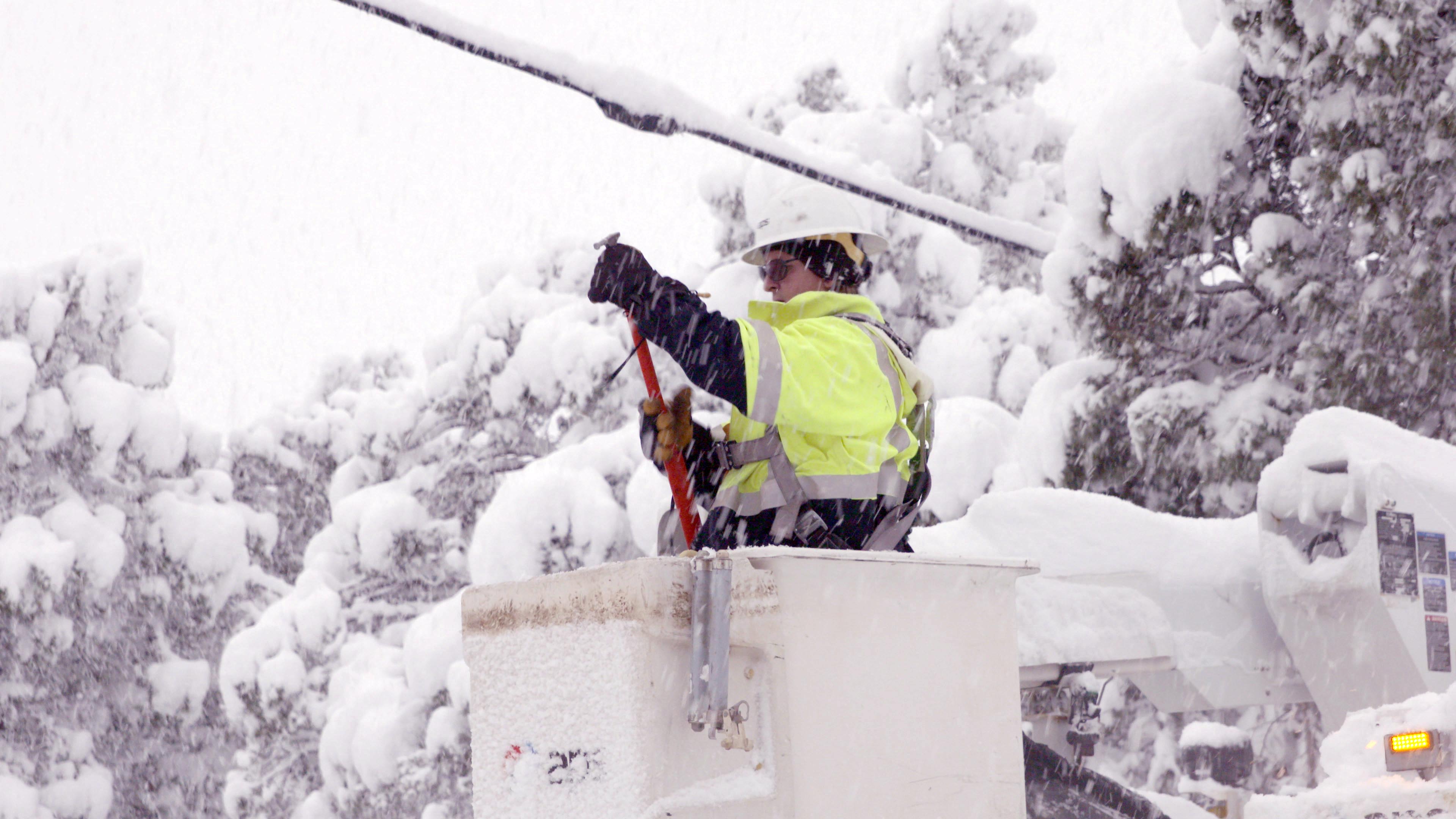 An APS lineman in a bucket working on a power line in the winter snow
