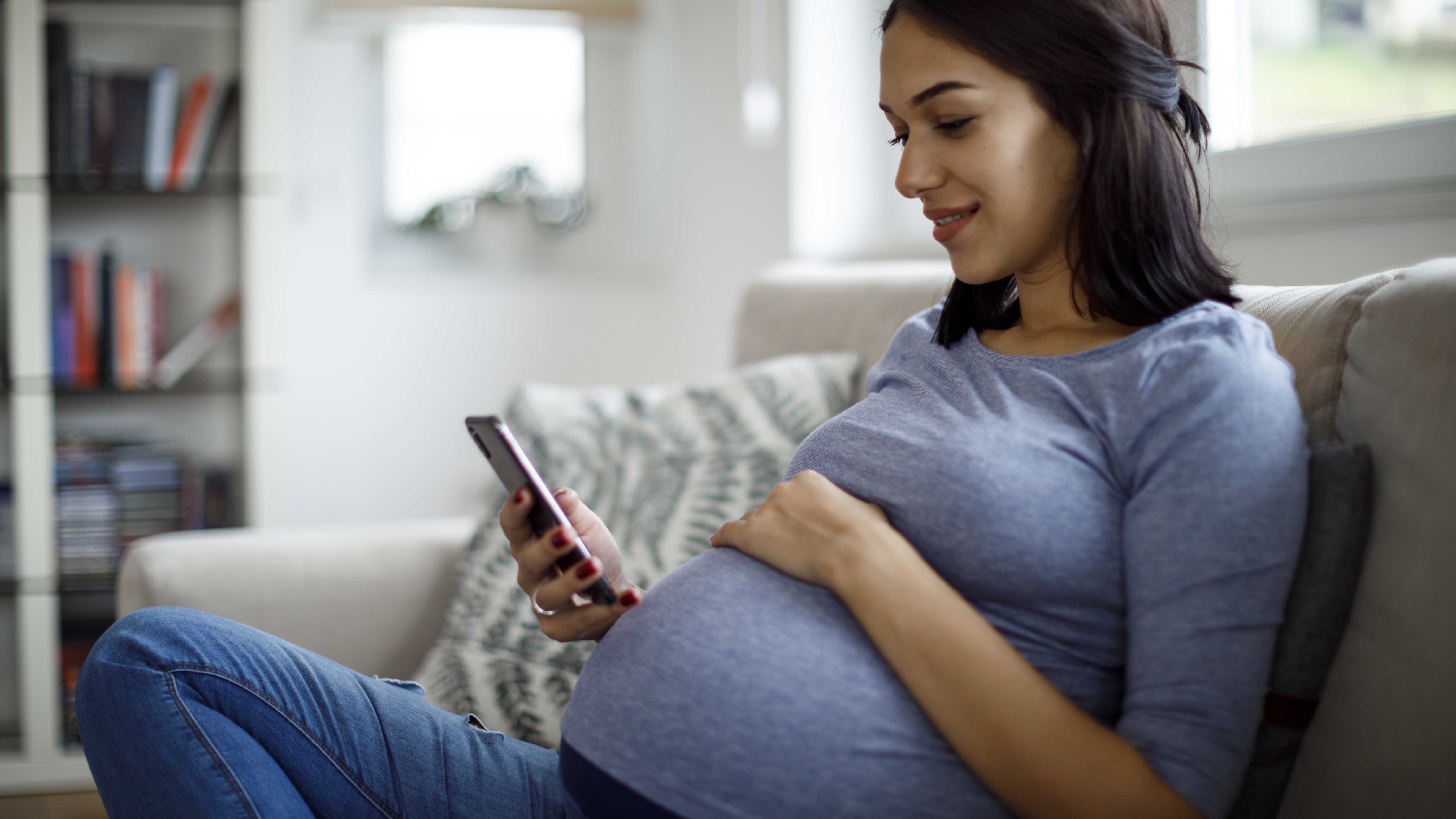  A pregnant woman relaxing on the couch and looking at her phone