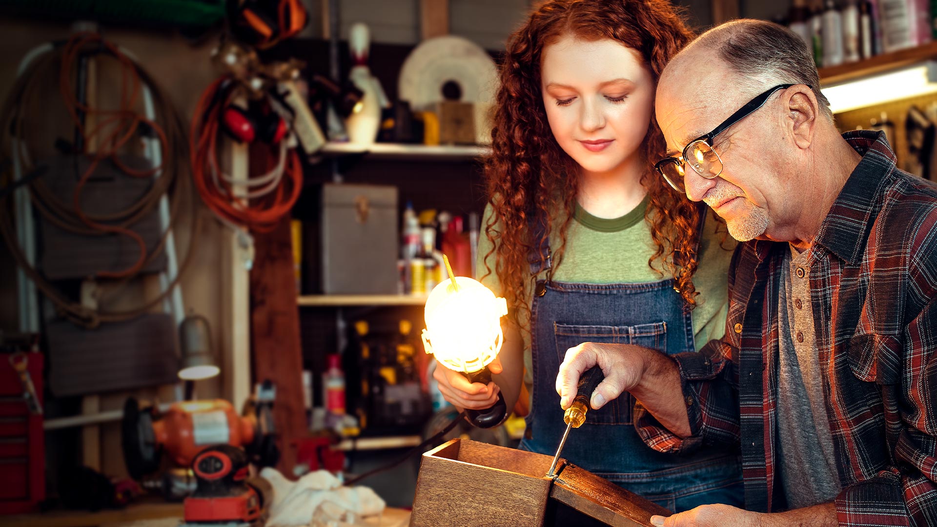Girl holding a light over a box that a man is working on in a workshop