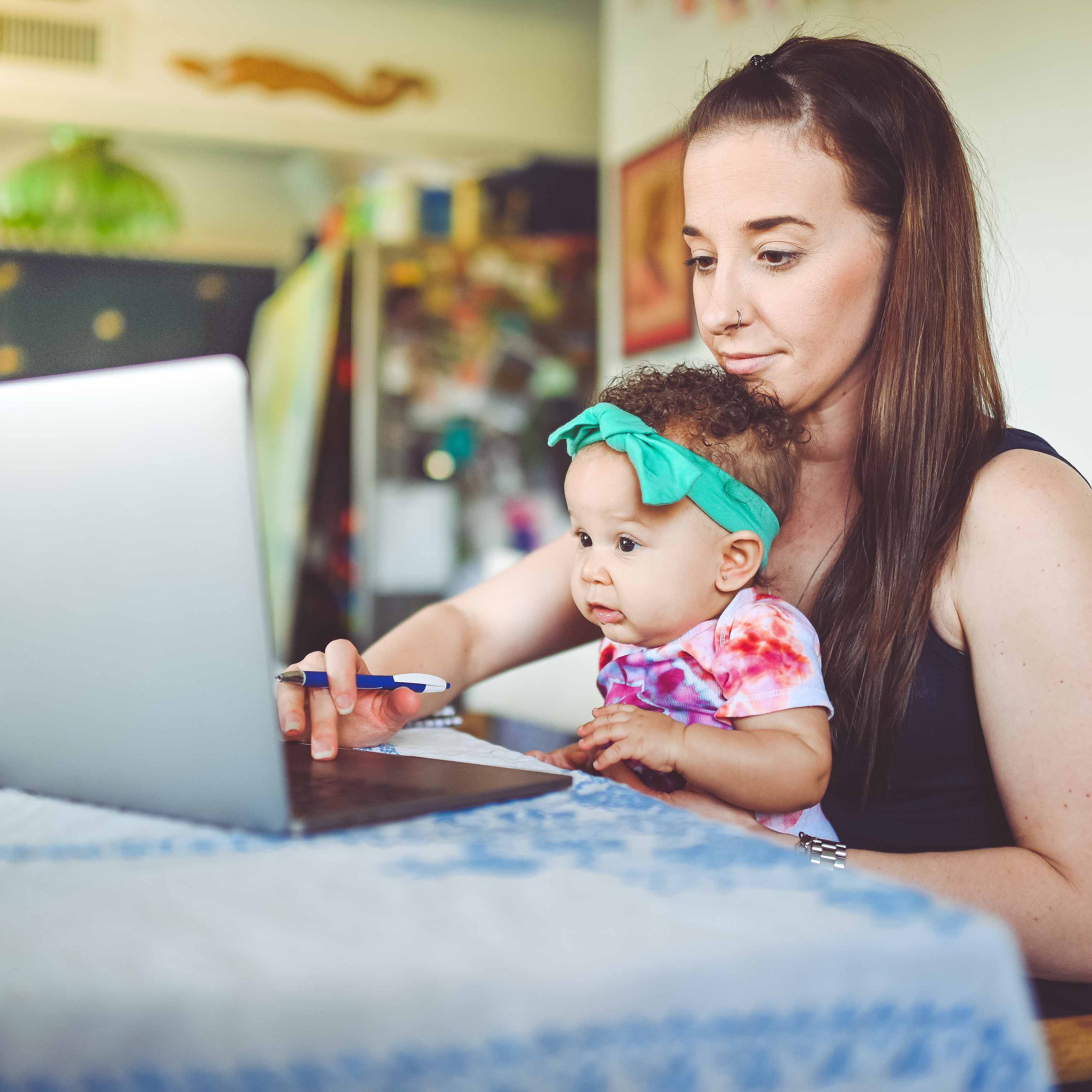A mom typing on a laptop while holding a small child on her lap