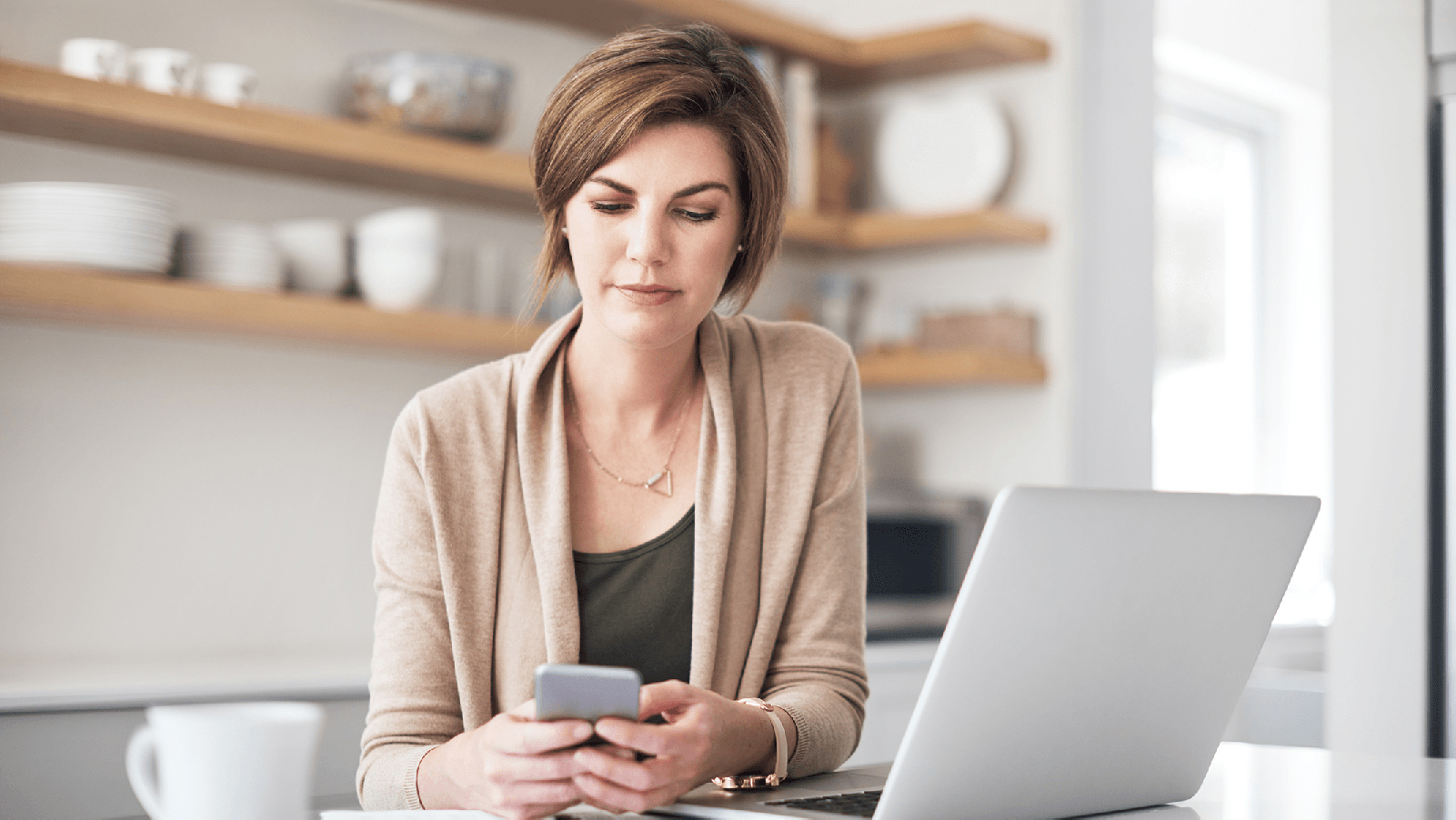 Woman looking at her phone in front of her laptop.