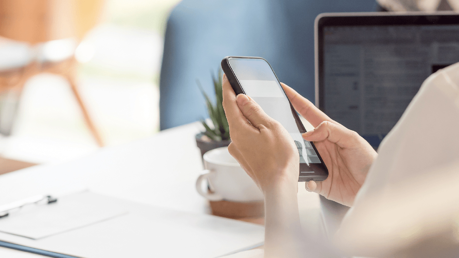 Woman looking at a cell phone while sitting at a desk. 