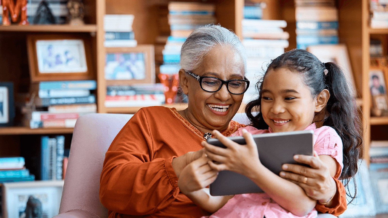 Grandma and her granddaughter smiling and looking at a tablet.