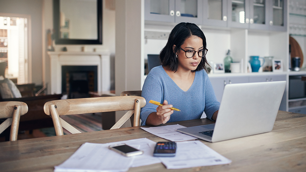 Woman sitting at table with laptop and papers.