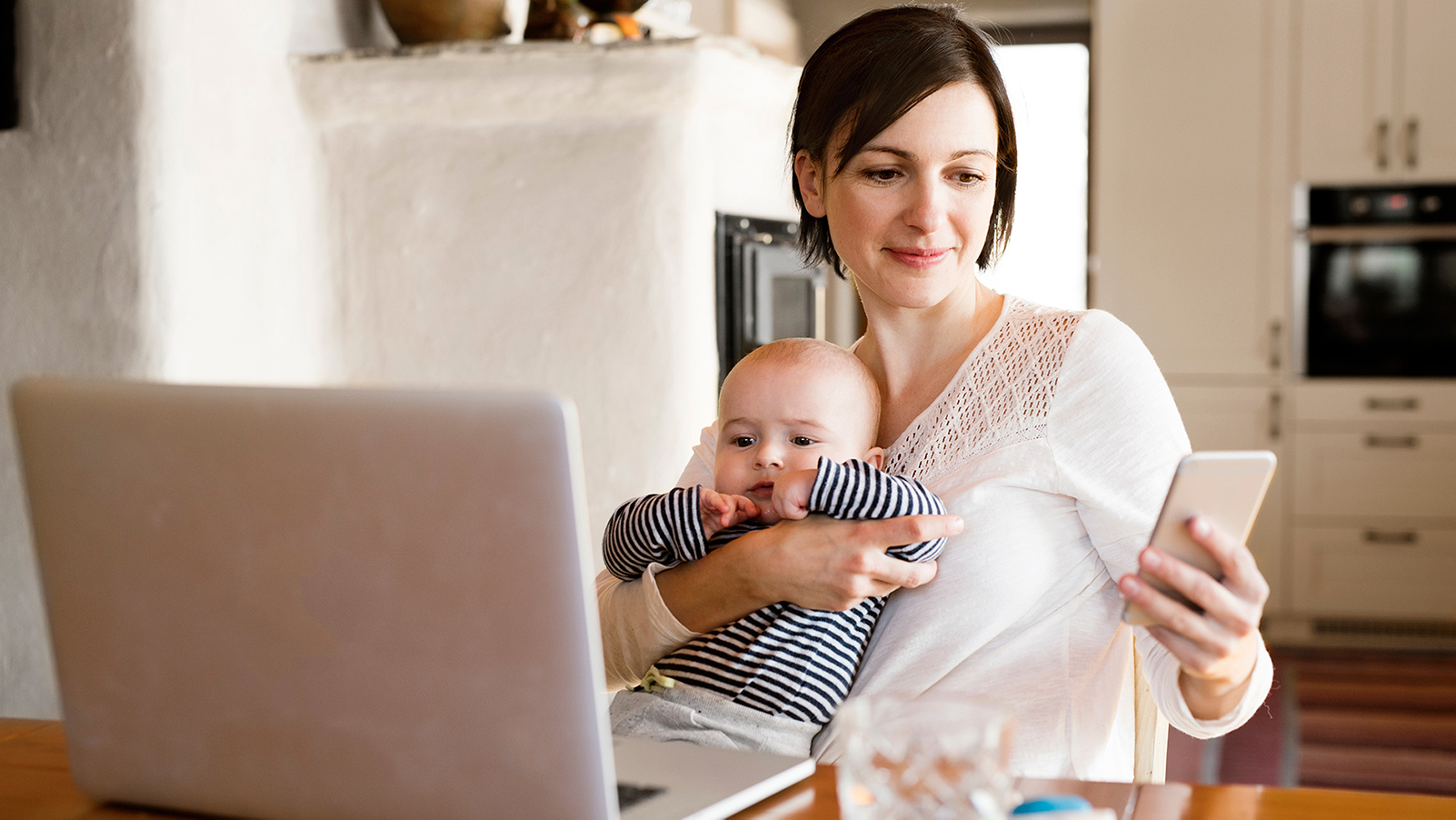 Woman with baby using cell phone and holding baby.